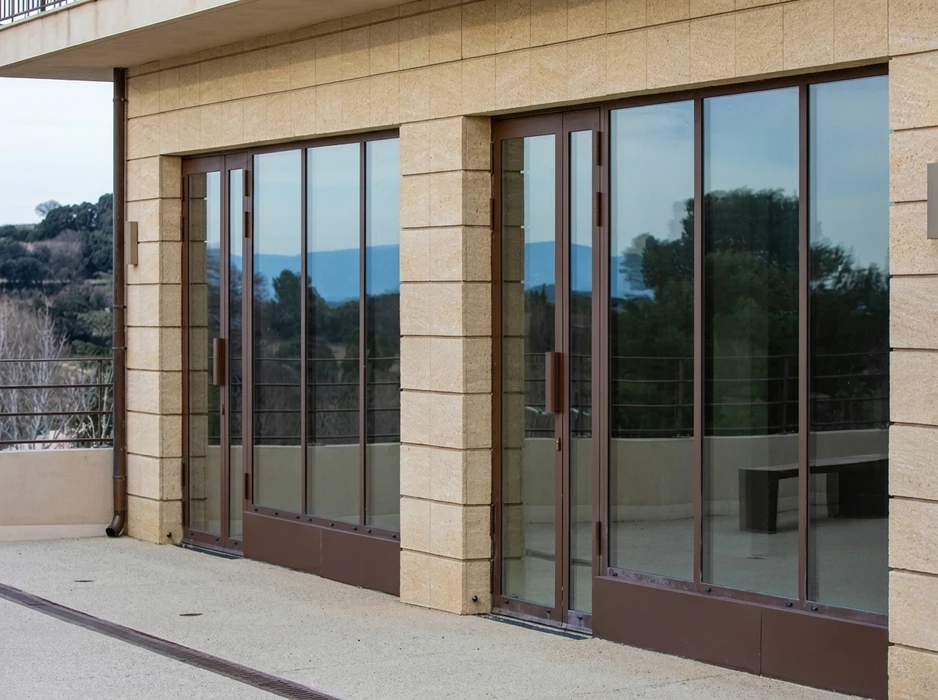 Façade extérieure d'un bâtiment en pierre calcaire beige, terrasse avec deux baies vitrées coulissantes à galandage