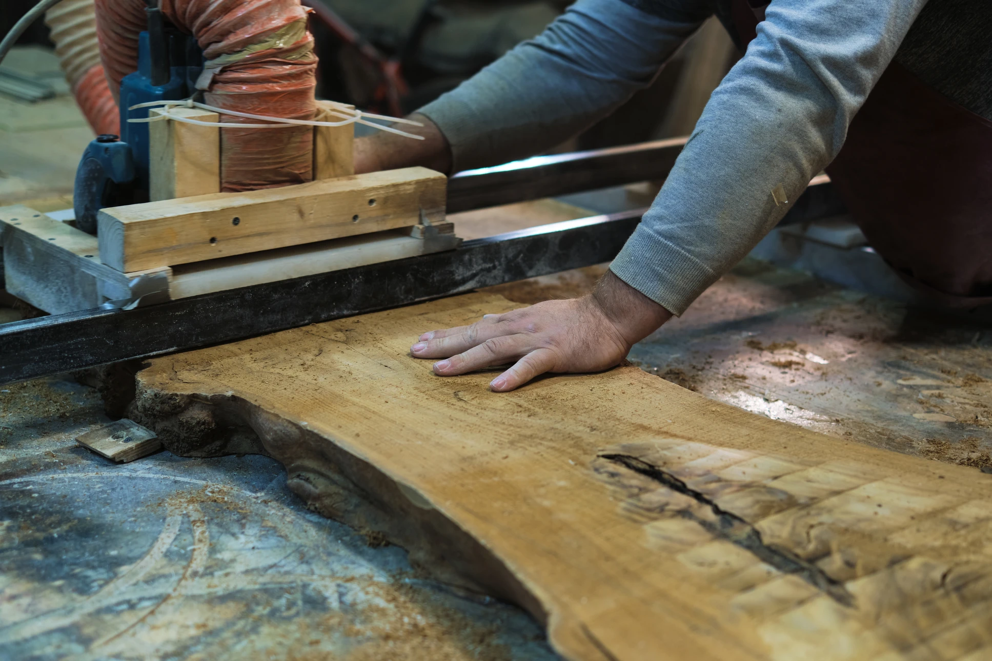 Atelier de menuiserie intérieur avec artisan travaillant sur scie à ruban, guidant planche de bois brut avec la main
